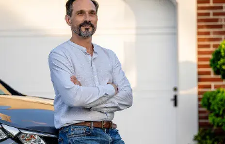 Un homme adossé à une voiture, les bras croisés